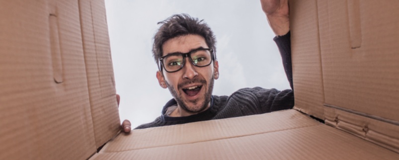Um jovem sorridente, de óculos, olha para dentro de uma caixa de papelão